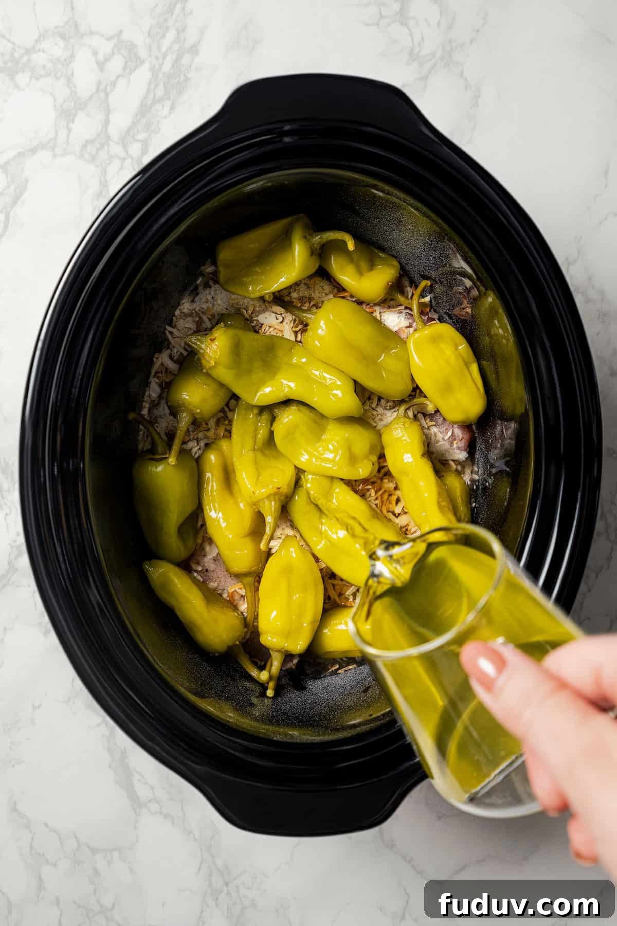 Mississippi chicken is an easy crock pot recipe with juicy chicken shredded in savory pepperoncini ranch sauce. Make it with 5 ingredients! Pepperoncini juice being poured over the peppers and chicken inside the crock pot.