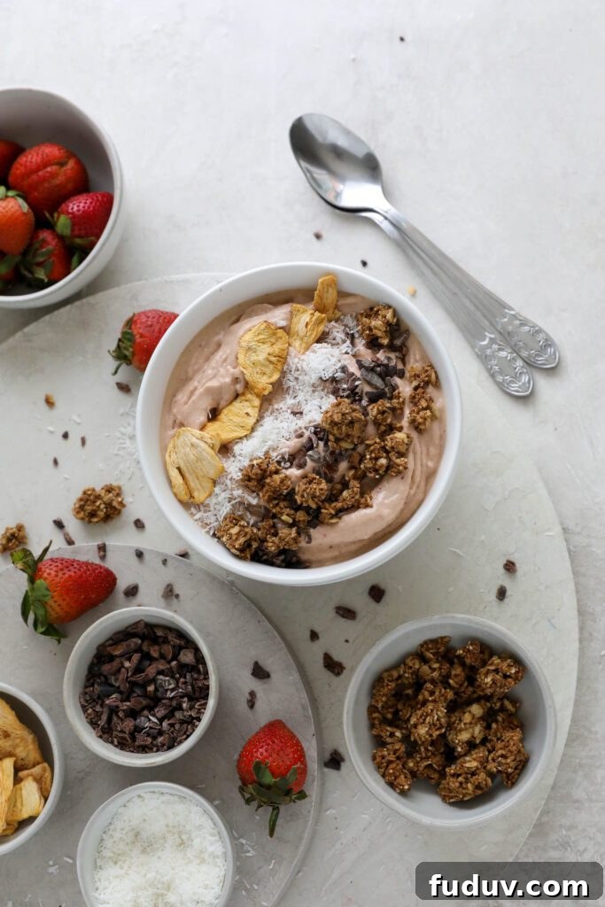 Strawberry Mango Smoothie Bowl served in bowl topped with dried pineapple, shredded coconut, and granola with fresh strawberries on the side