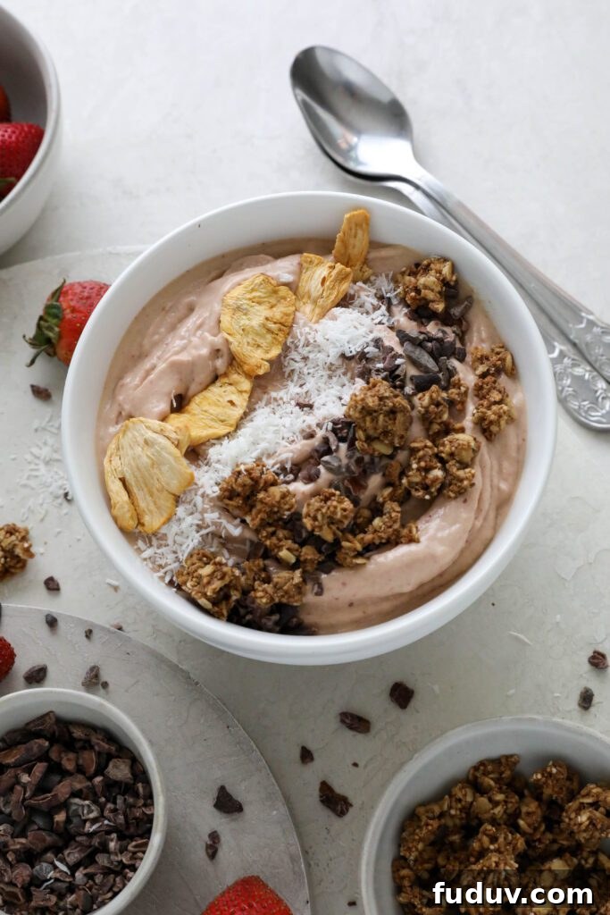Strawberry Mango Smoothie Bowl served in bowl topped with dried pineapple, shredded coconut, and granola with fresh strawberries on the side