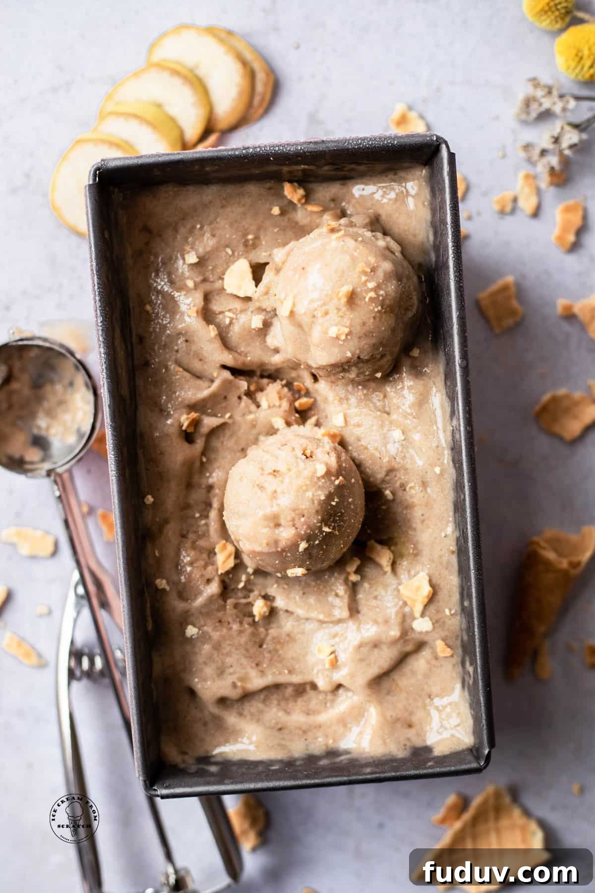 Creamy Banana Ice Cream Recipe: No-Added-Sugar Frozen Treat 5 a metal loaf pan filled with banana nice cream. Two scoops have been made and placed on top. Crumbled sugar cones are sprinkled over and around the pan.