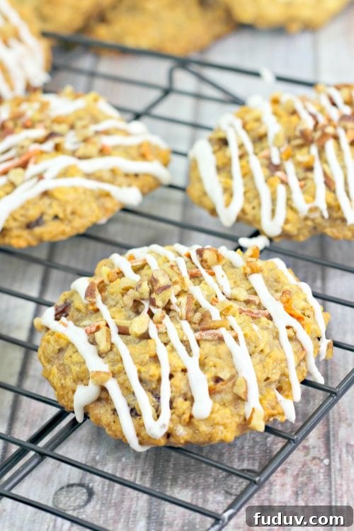 carrot cake cookies drizzled with cream cheese frosting on a black wire rack.