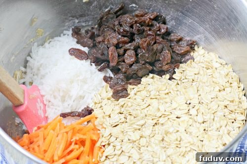 a silver bowl containing oats carrots, raisins, and coconut.