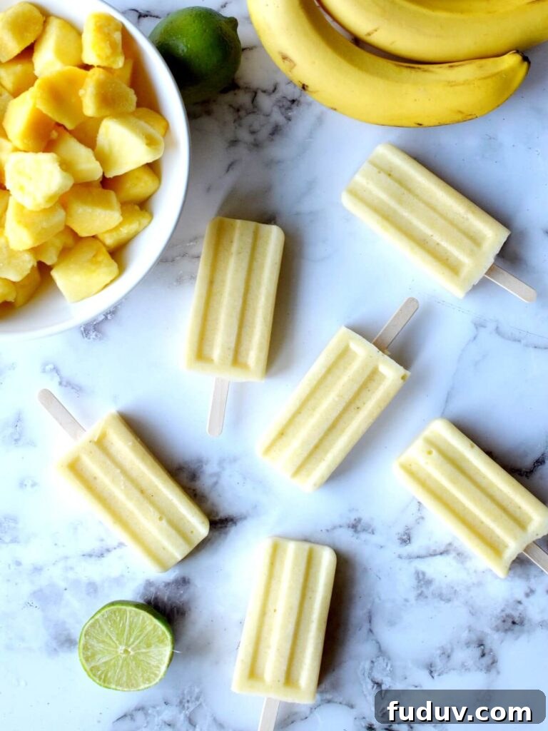pineapple popsicles laying on a counter with limes, bananas and pineapple around it