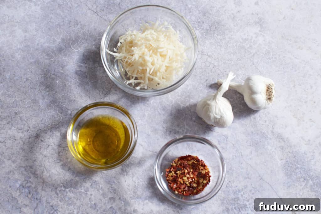 Two heads of garlic with three small glass bowls of parmigiano cheese, olive oil, and crushed red pepper.