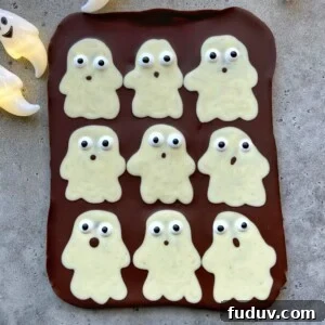 A slab of chocolate topped with nine white chocolate ghost shapes, each with candy eyes and different mouth expressions, arranged in a grid on a gray surface—perfect for fun food recipes or festive bites.