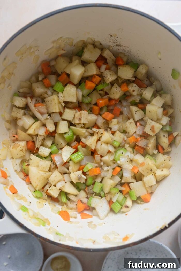 Potato, carrot, celery, onion and herbs cooking in a pot.