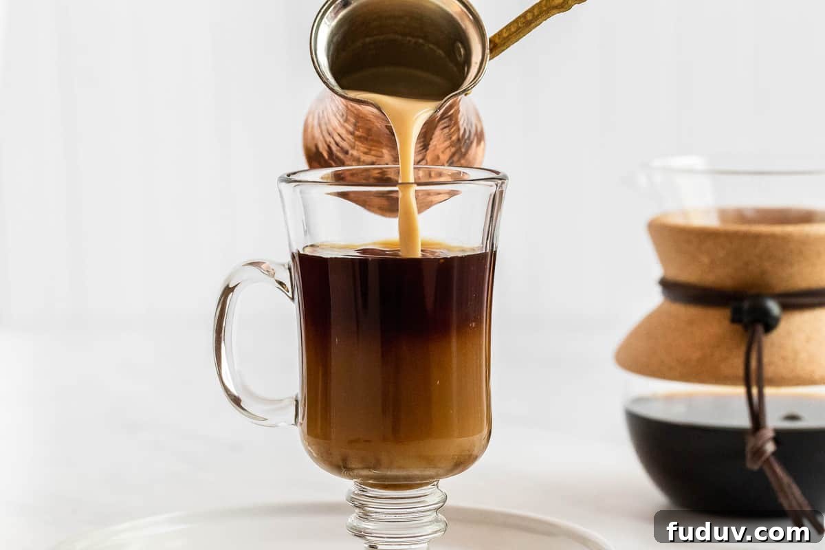 How to Make a Rich Caramel Latte at Home in Minutes 5 Frothed milk pouring into clear coffee mug.