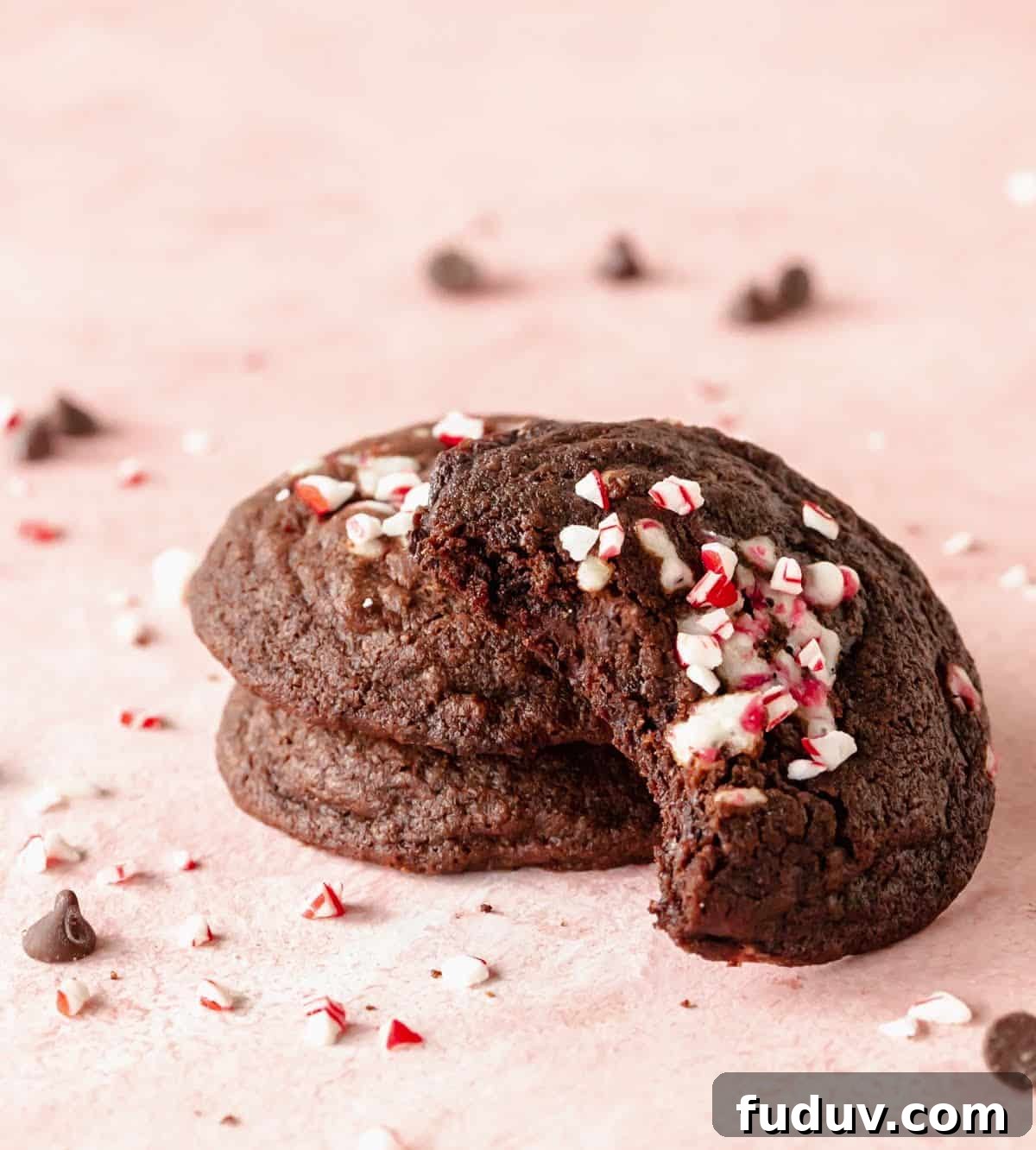 Stack of three chocolate peppermint cookies, one bitten, pink background.