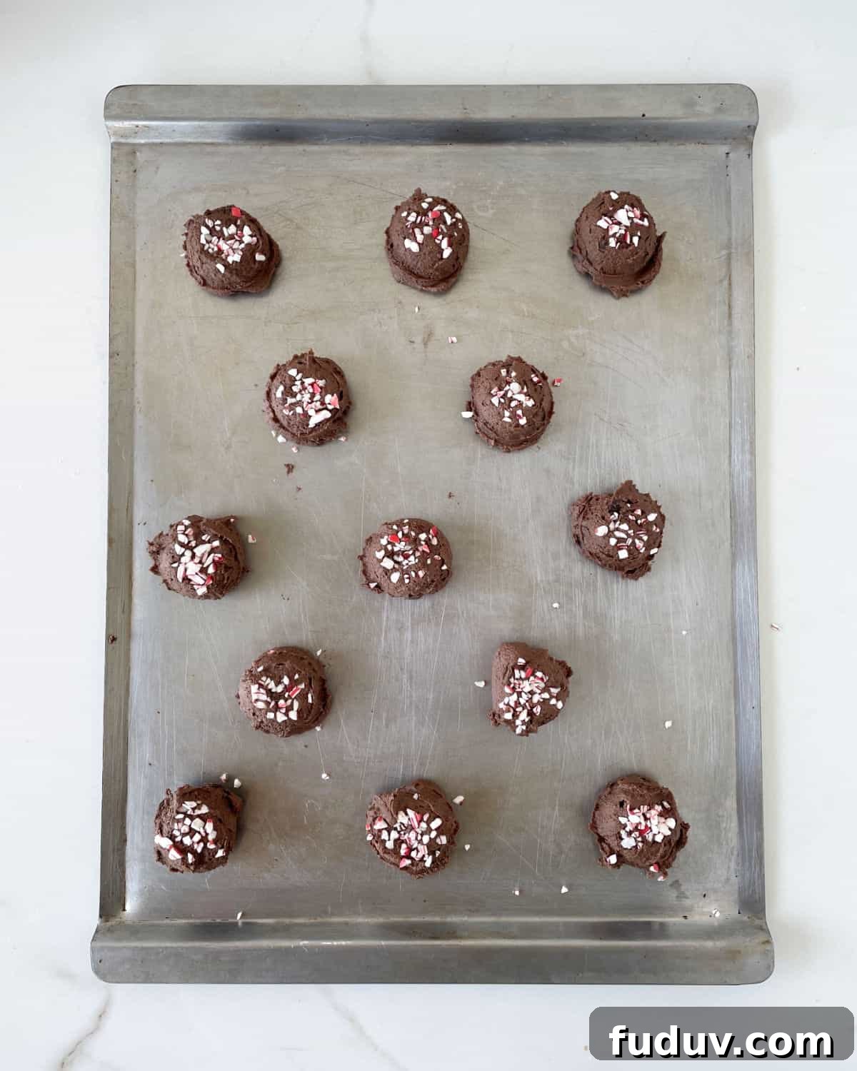 Metal baking sheet with chocolate cookie dough balls with crushed peppermint candy. Top view.
