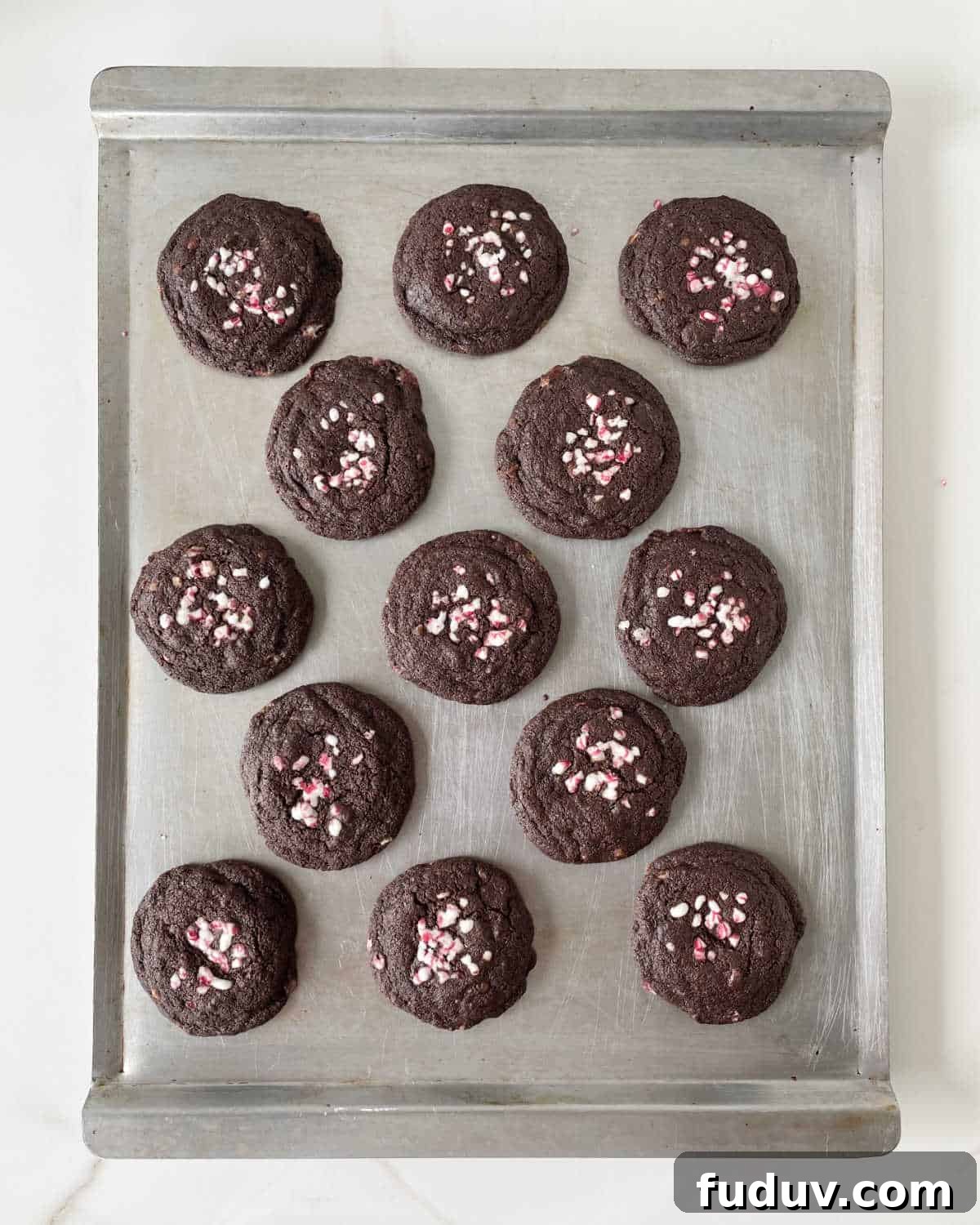 Top view of baked chocolate cookies with crushed peppermint candy on a metal baking sheet.
