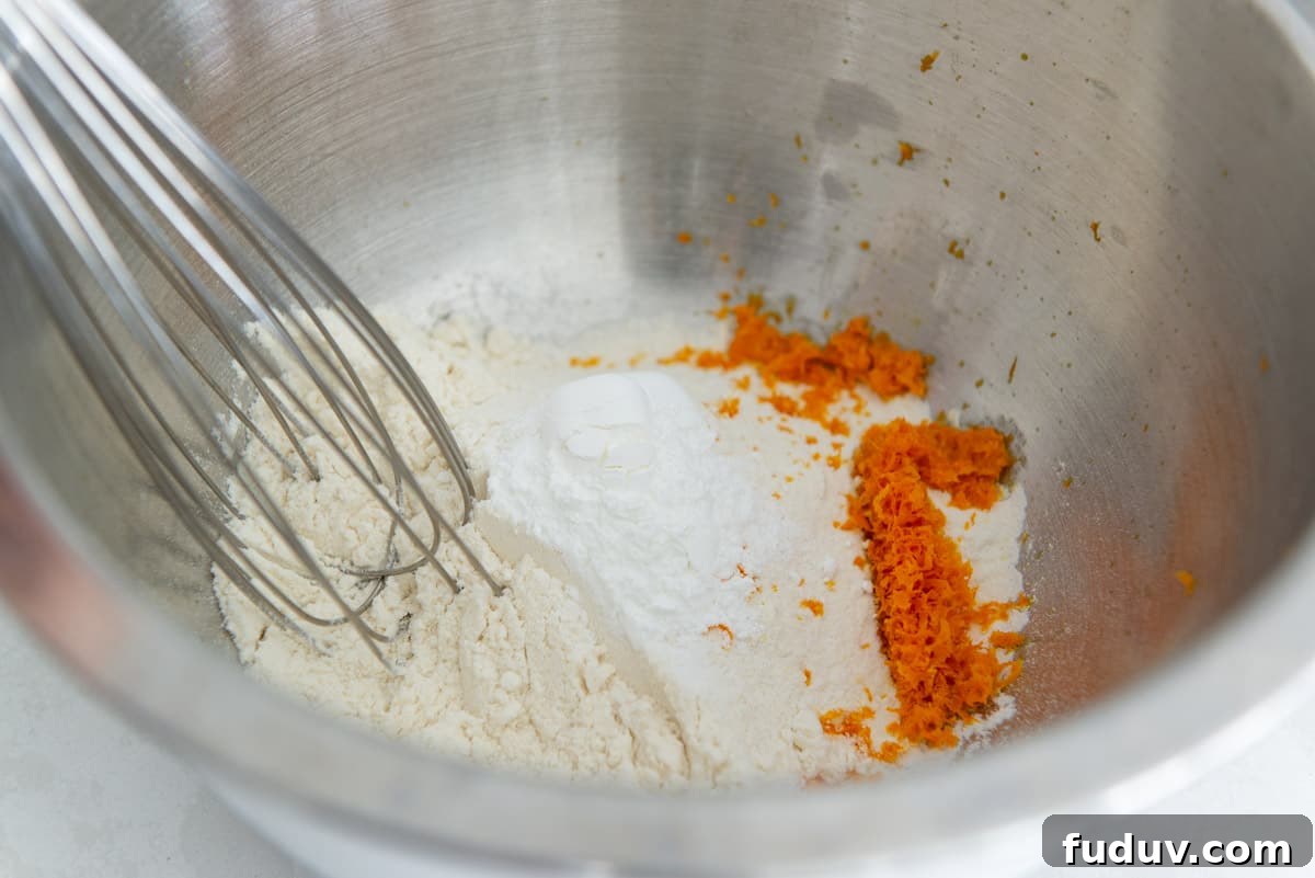 Flour, baking powder, salt, and orange zest in a bowl with a whisk