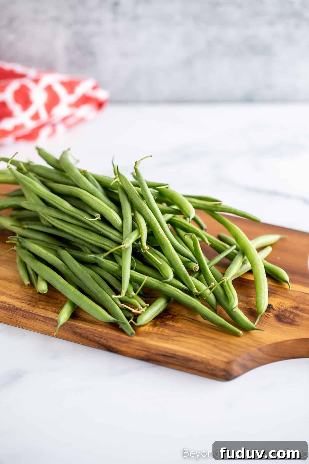 Fresh green beans on a wooden cutting board.