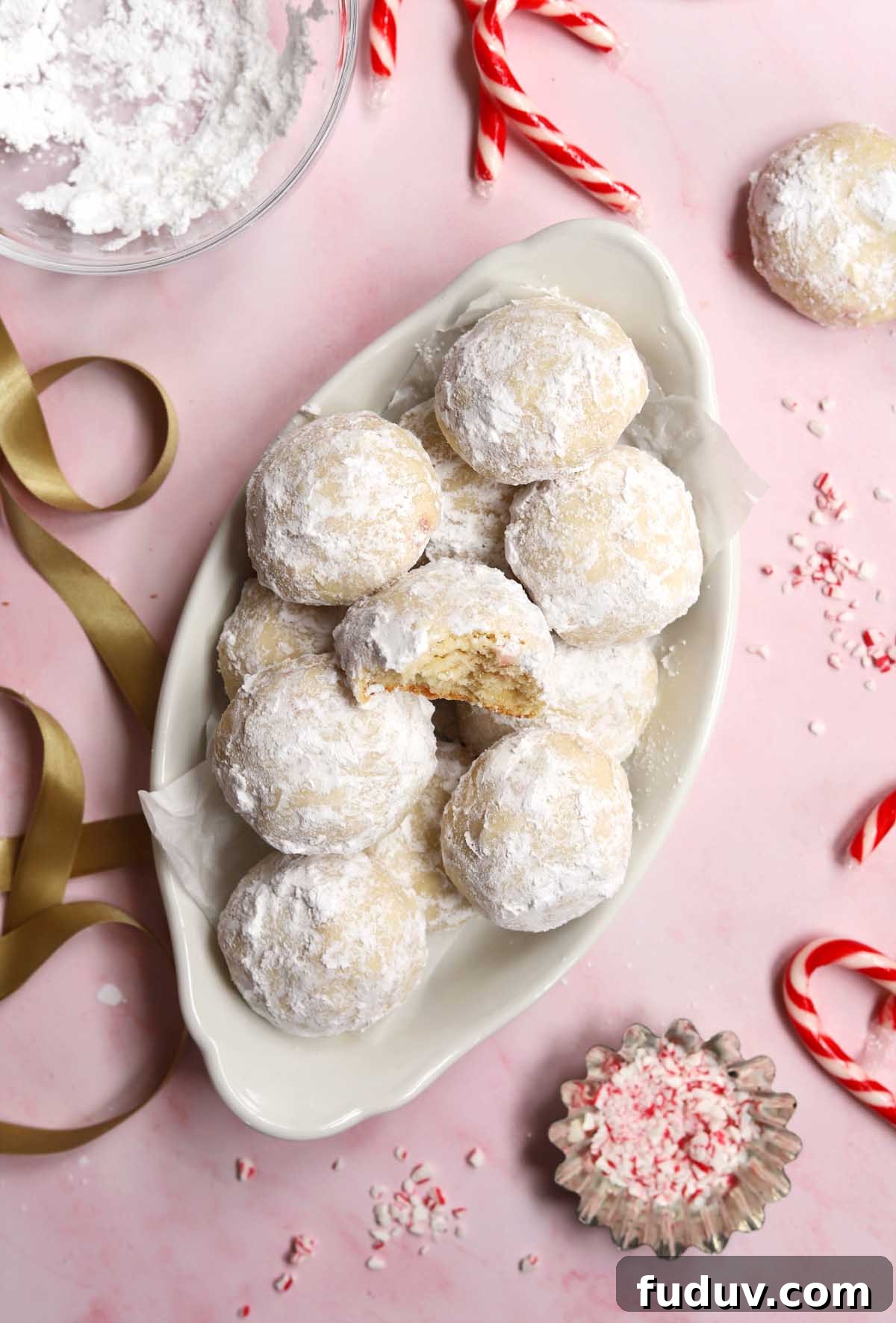 top view of peppermint snowball cookies in a serving dish with bite showing tender insides
