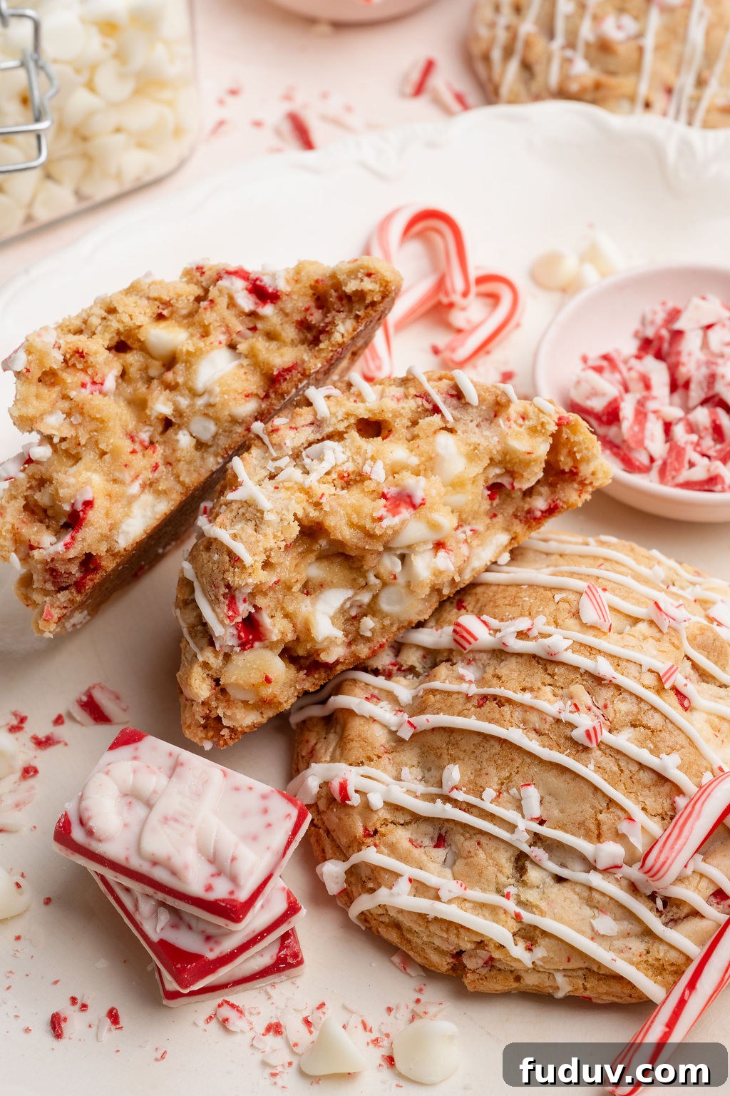 White Chocolate Peppermint Cookies Recipe for the Holidays 15 White chocolate peppermint cookies on a plate with a stacked peppermint bark square, candy canes, and crushed peppermint scattered around.