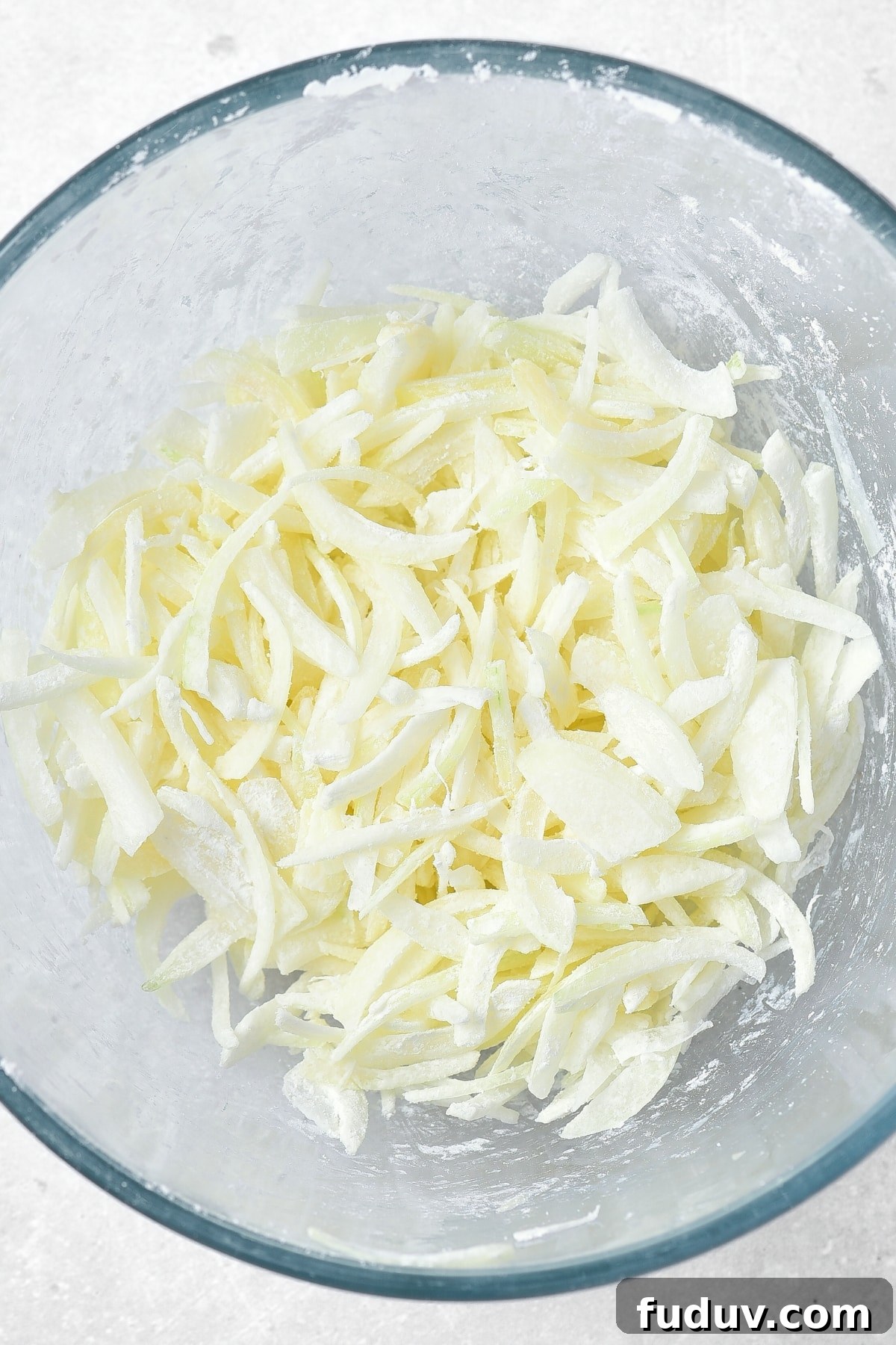 Corn starch coated onion slices in glass bowl.