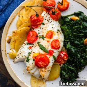 Baked cod with lemon potatoes and cherry tomatoes on white plate.