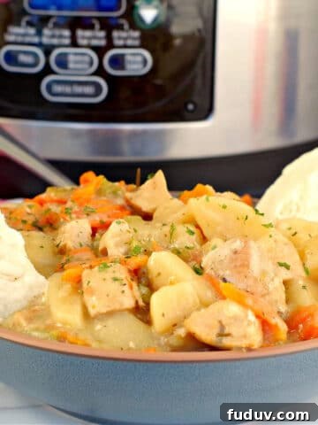 crockpot chicken stew in a blue bowl with biscuits on the side and a slow cooker in the background