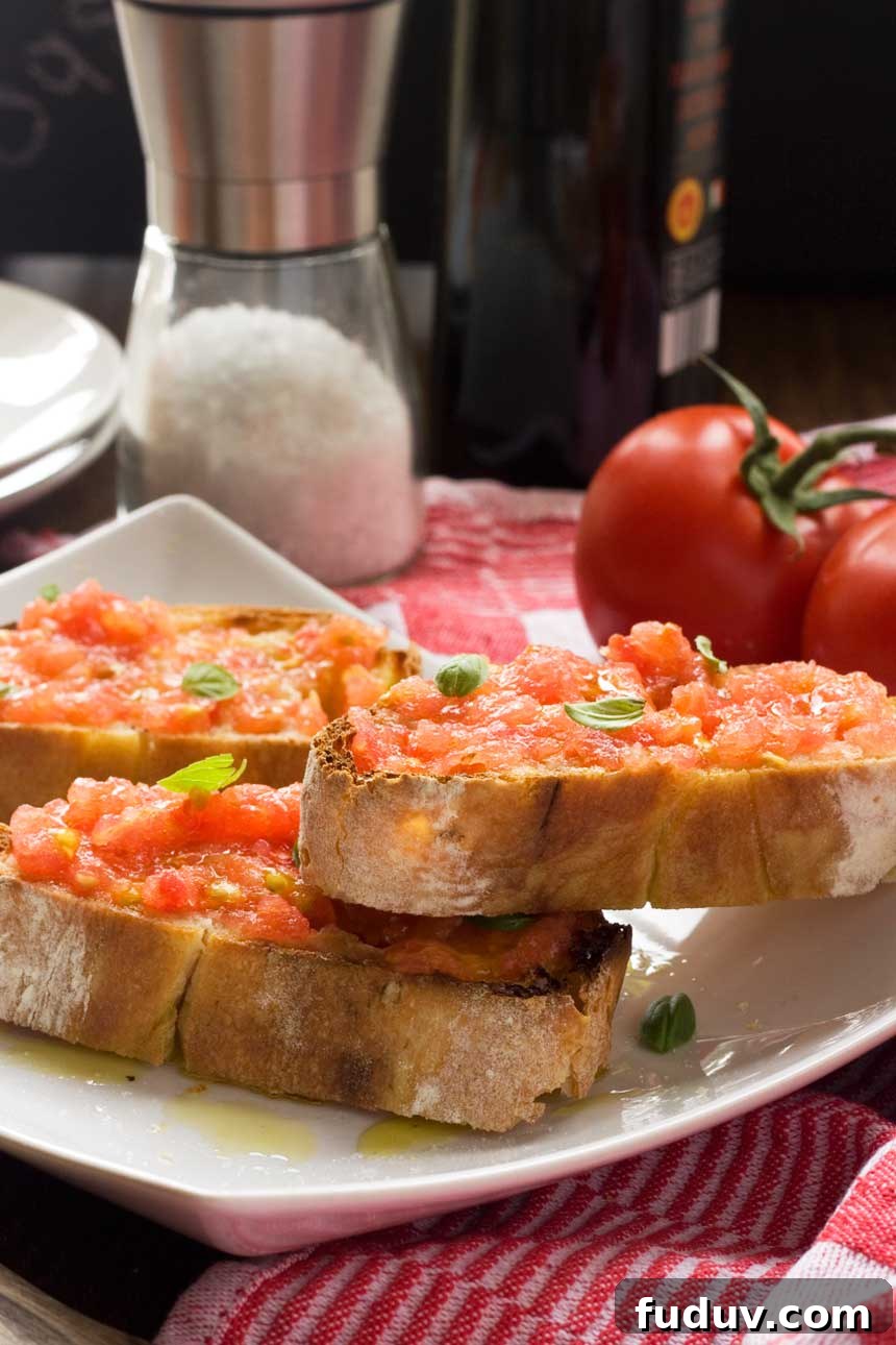 Pan con Tomate: Classic Spanish Tomato Toast Recipe 6 Tomato bruchetta piled onto a plate with ingredients in the background.