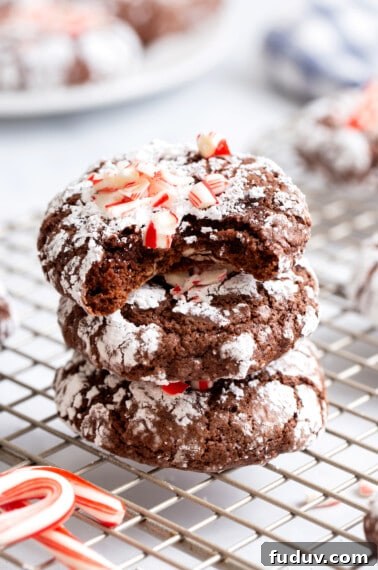 Three chocolate mint crinkle cookies stacked on top of each other, the top cookie missing a bite.