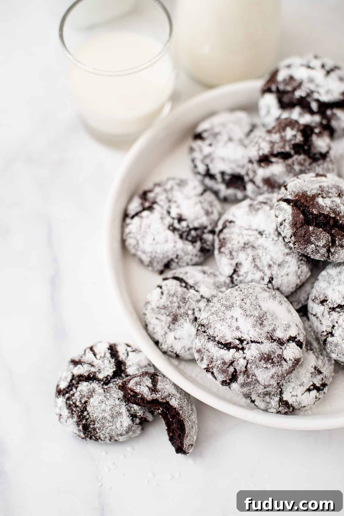 chocolate crinkles served on a white round plate with two cookies sitting next to the plate on a marble countertop.