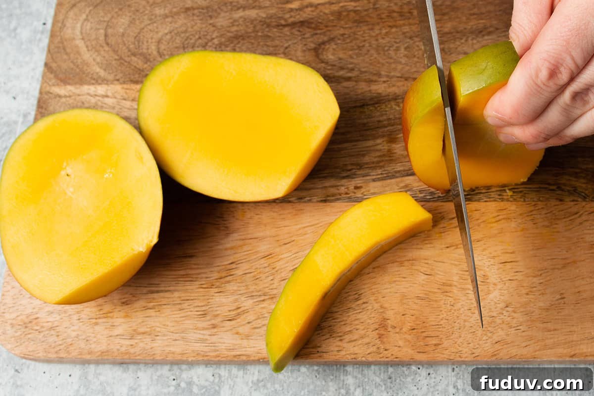 A mango with 3 pieces already removed and the last side being cut off.