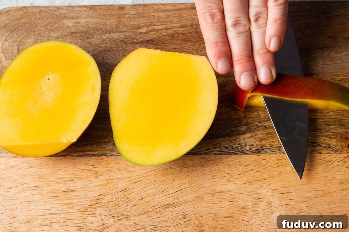 A knife cutting away the skin from a small piece of mango.