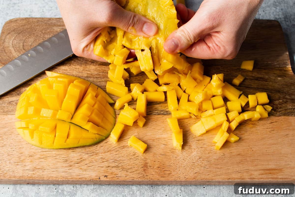 Two hands removing the diced mango from the skin.