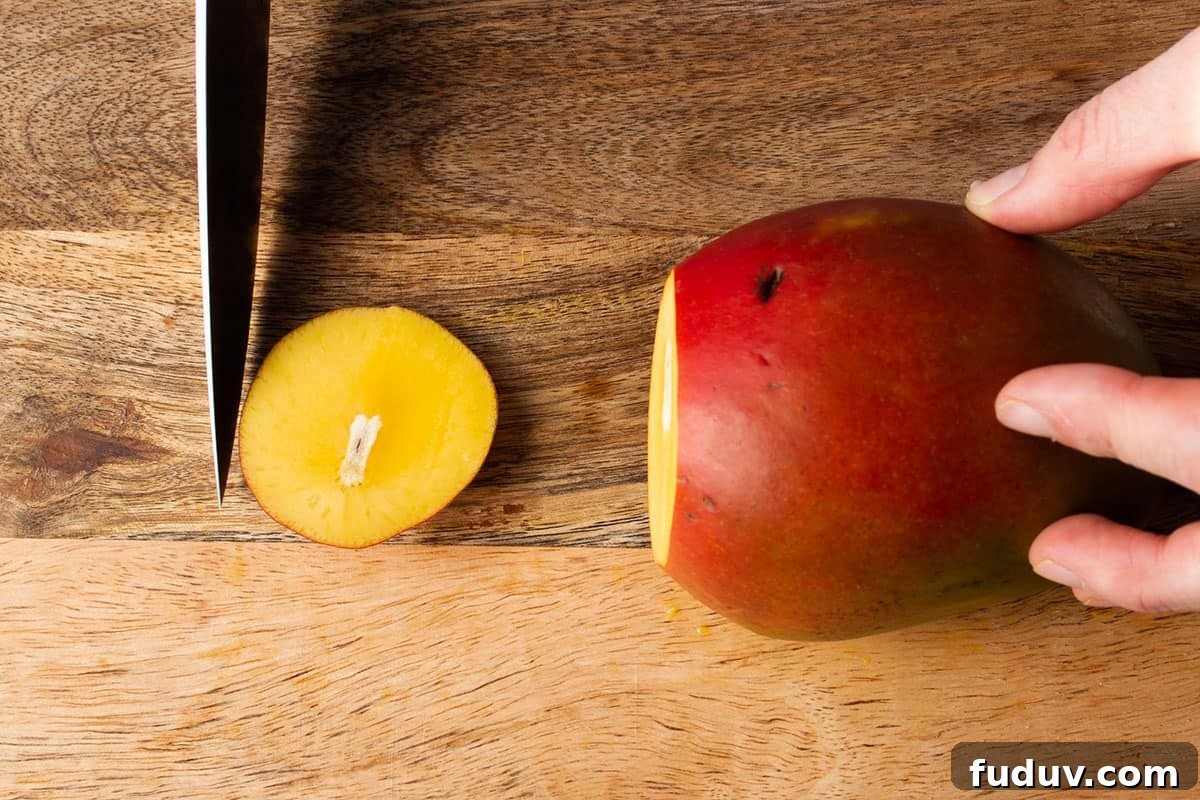 A knife cutting off the bottom piece of a mango.
