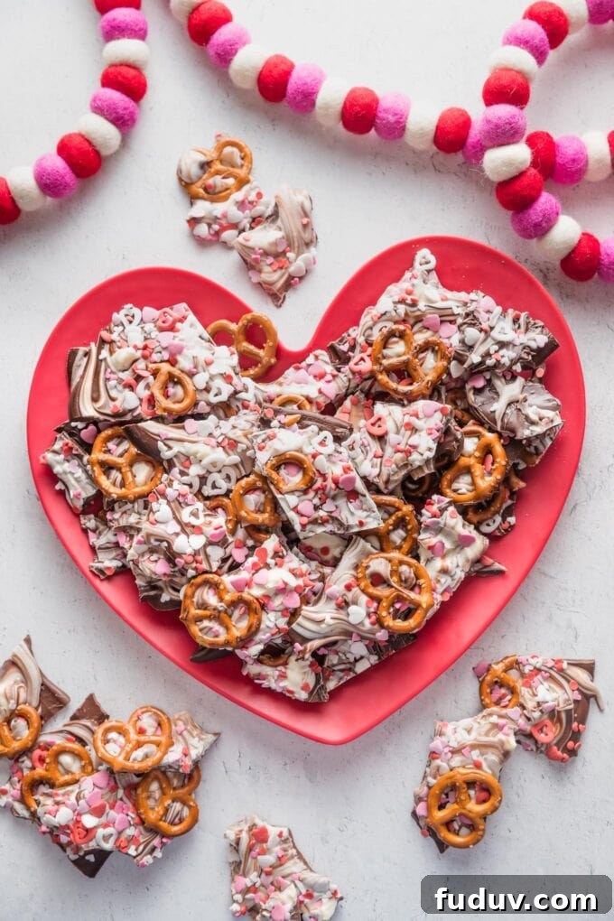 Red heart-shaped plate piled high with Valentine's-themed chocolate pretzel bark.