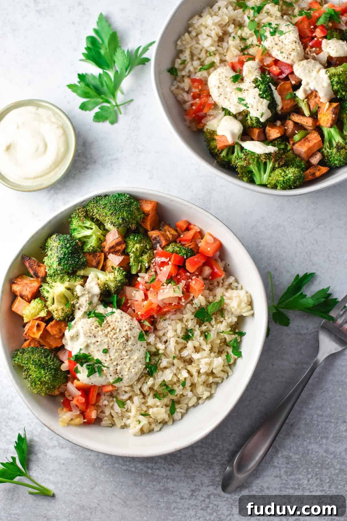 Two sweet potato bowls filled with rice, broccoli, and veggies next to a small bowl of creamy tahini sauce.