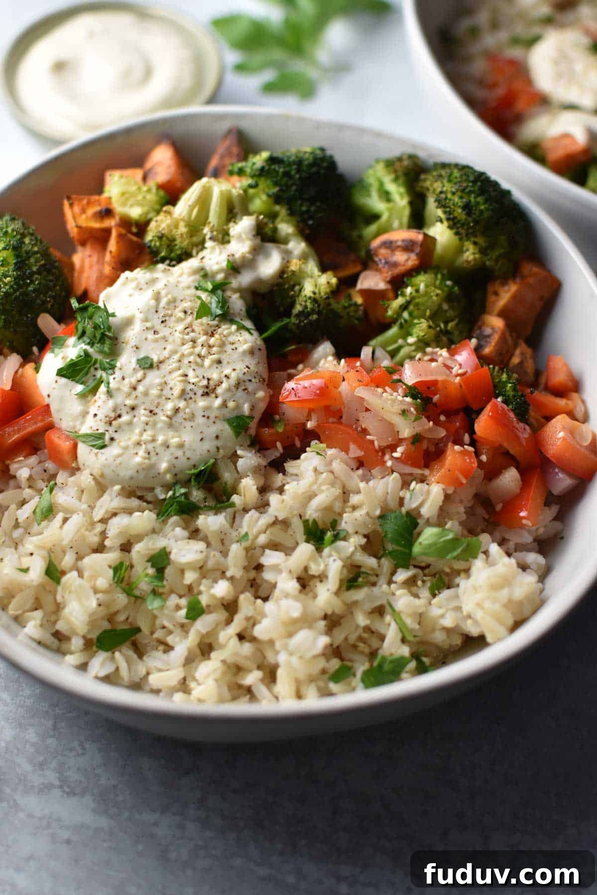 A bowl with sweet potatoes, broccoli, red pepper, rice, and a tahini sauce on top with sesame seeds.
