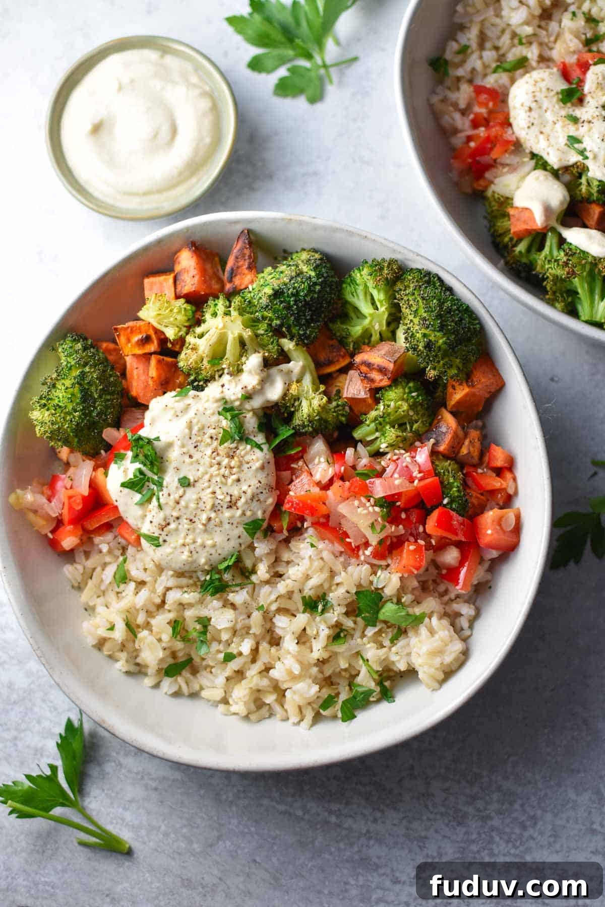 Two prepped bowls filled with roasted broccoli and sweet potatoes next to a small dipping sauce bowl.
