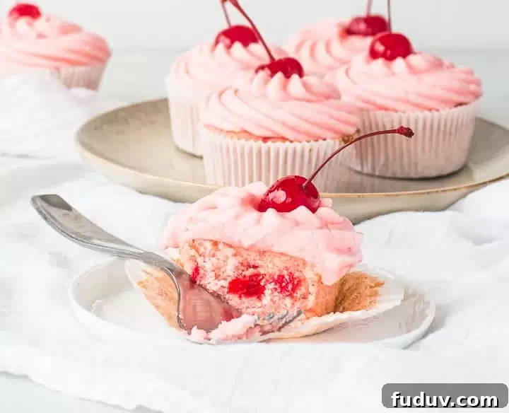 cherry cupcake on a plate with a fork taking a bite out of it and more cupcakes behind it