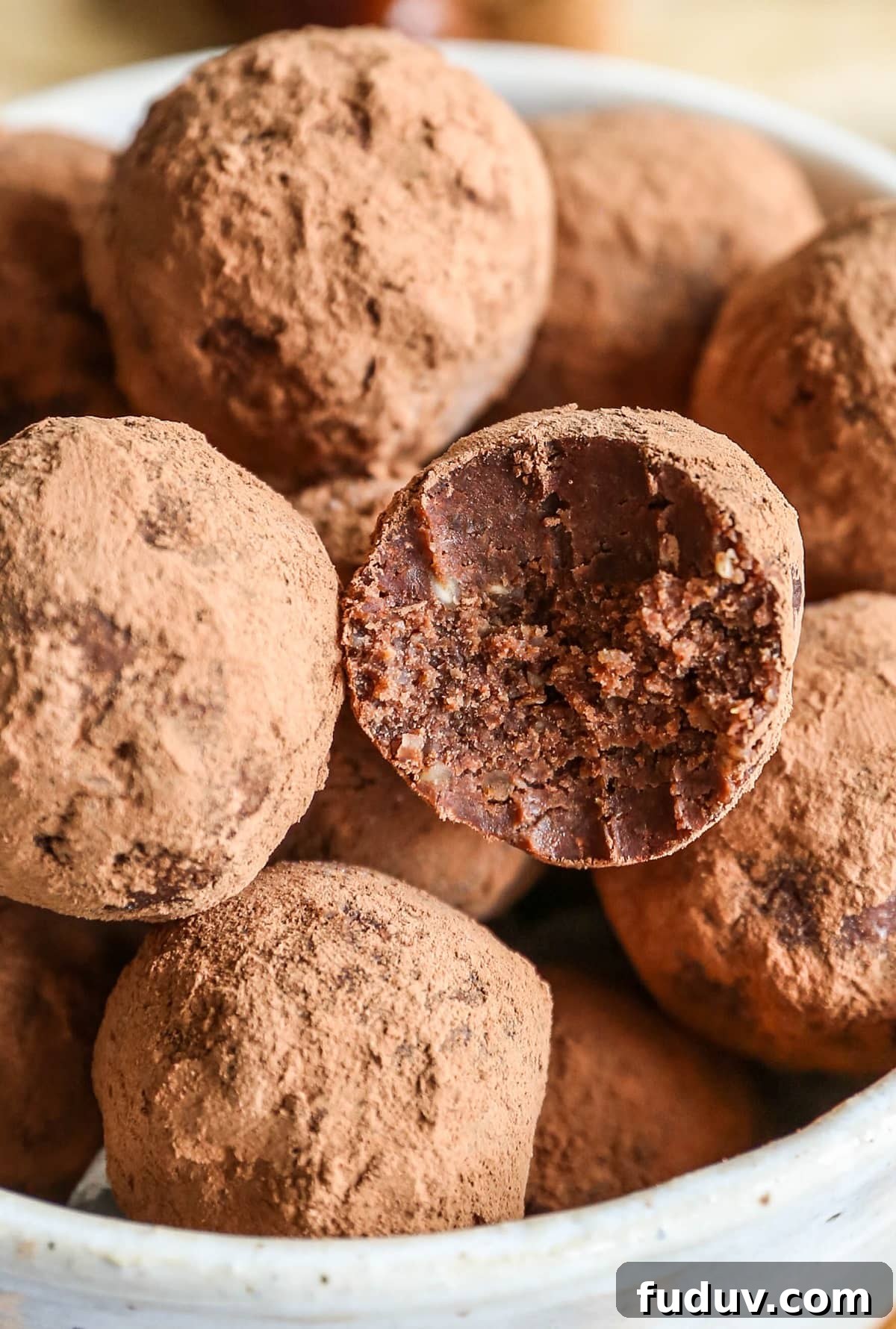 5-Ingredient Chocolate Date Energy Bites for Quick Fuel 4 Bowl of chocolate date energy bites with one of the balls with a bite taken out.