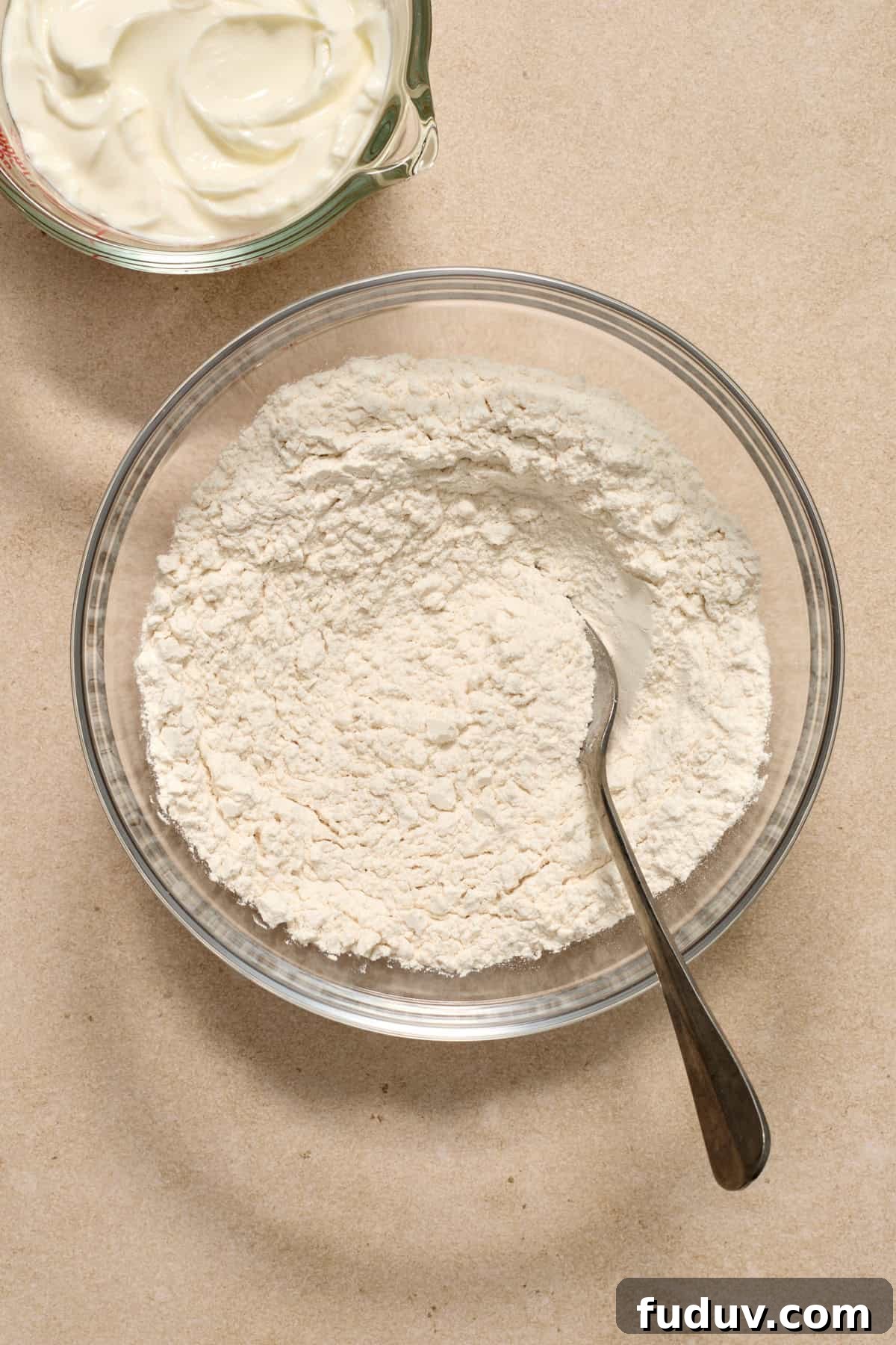 Dry ingredients in glass mixing bowl with spoon.