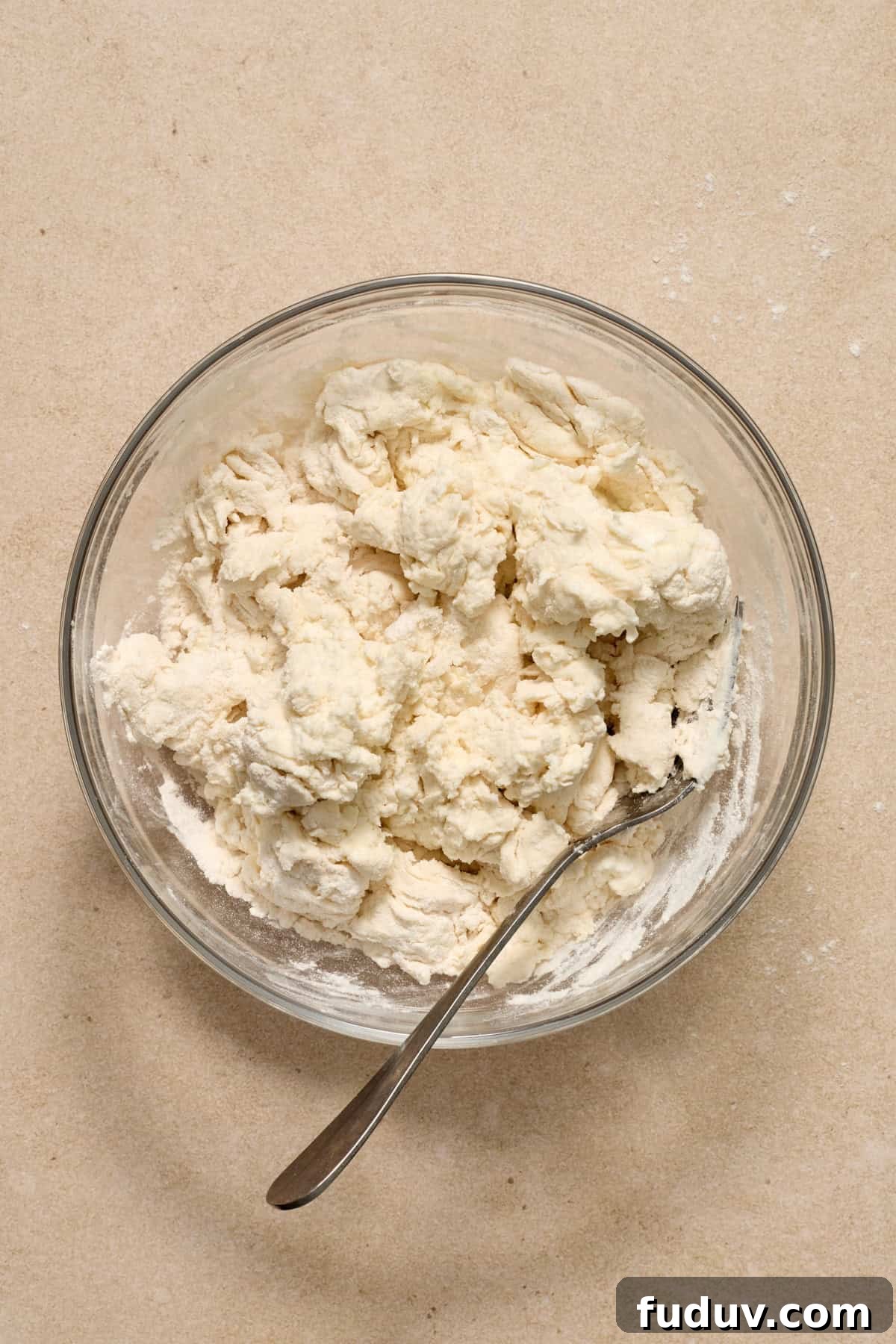 Greek yogurt bagel dough mixture in glass bowl with metal spoon.