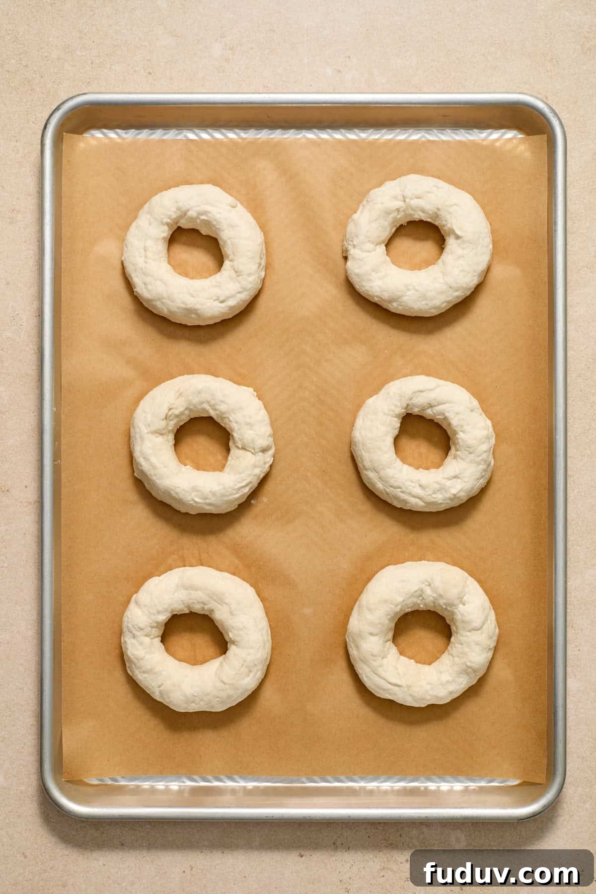 Bagels formed and arranged on parchment paper lined cookie sheet.