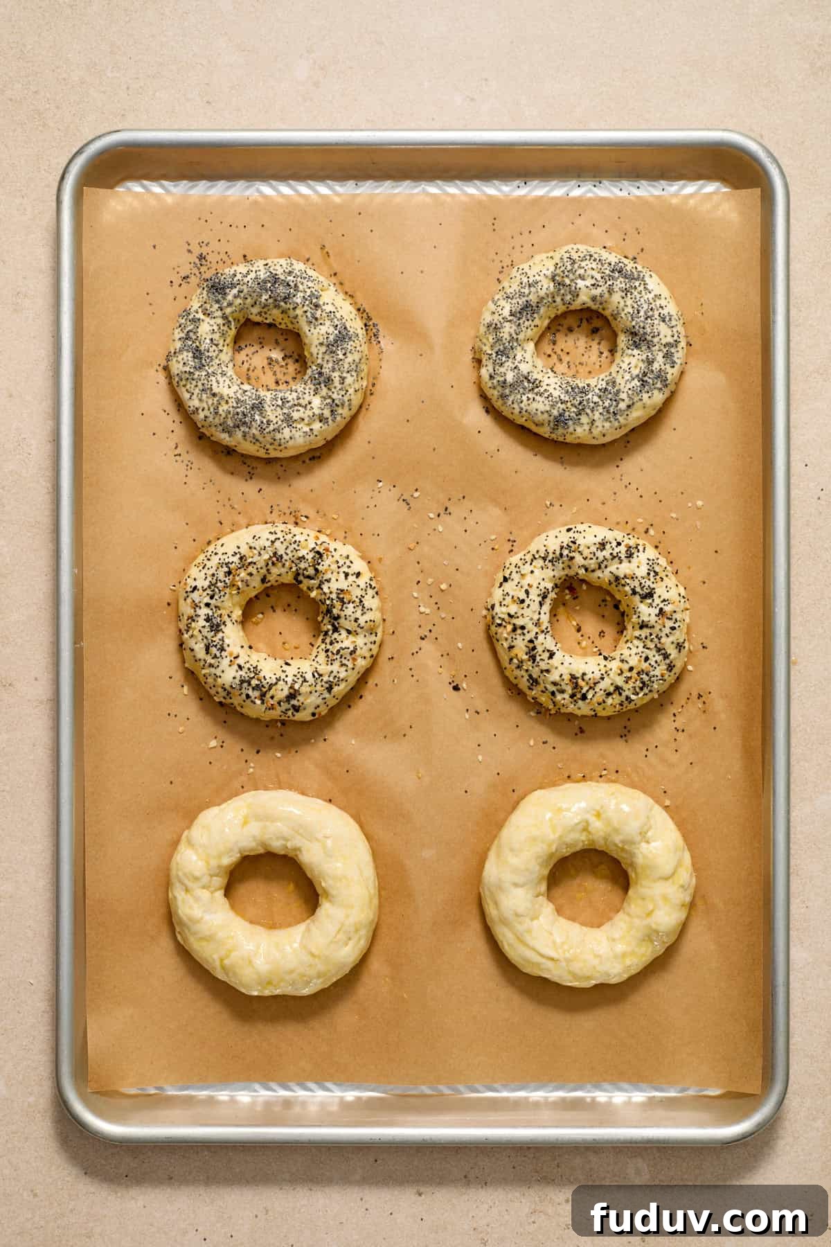 Egg washed bagels with poppy seeds and other ingredients on top.