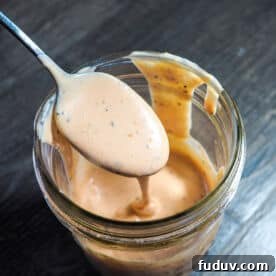 A jar of homemade raising canes sauce dripping off of a spoon.