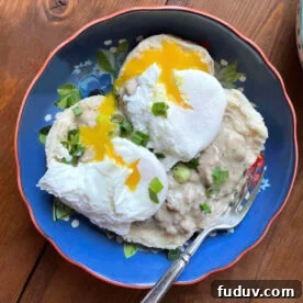 A blue bowl with two biscuits topped with sausage gravy and two poached eggs.