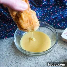 A chicken nugget being dunked into a small glass bowl of copycat chick-fil-a sauce.