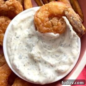 A small bowl of homemade tartar sauce with a fried shrimp in it.