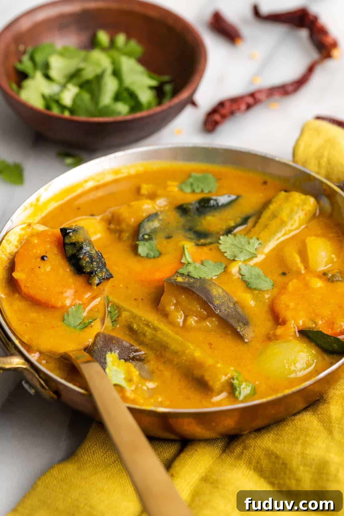 Bowl of sambar with small bowl of cilantro leaves and dried chilis in background