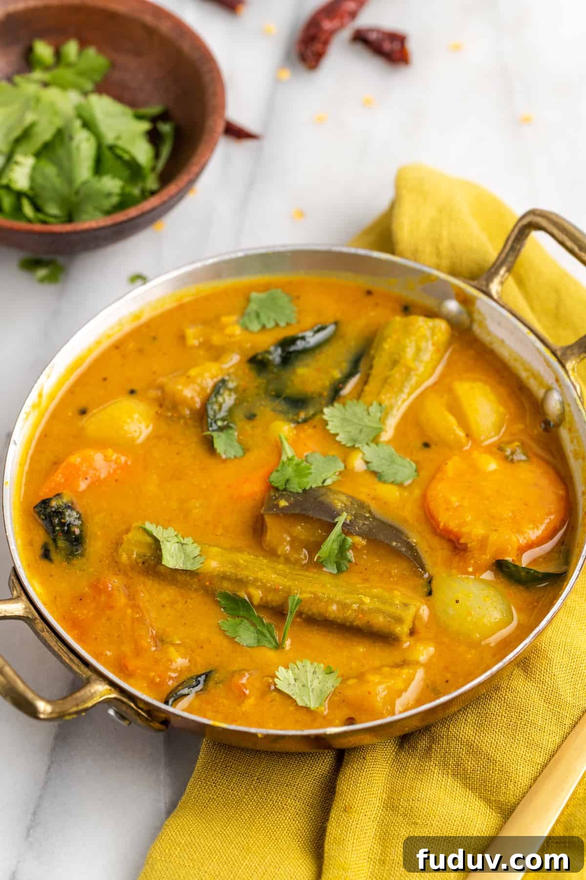 Vegan sambar in gold serving dish, with cilantro leaves scattered on top for garnish