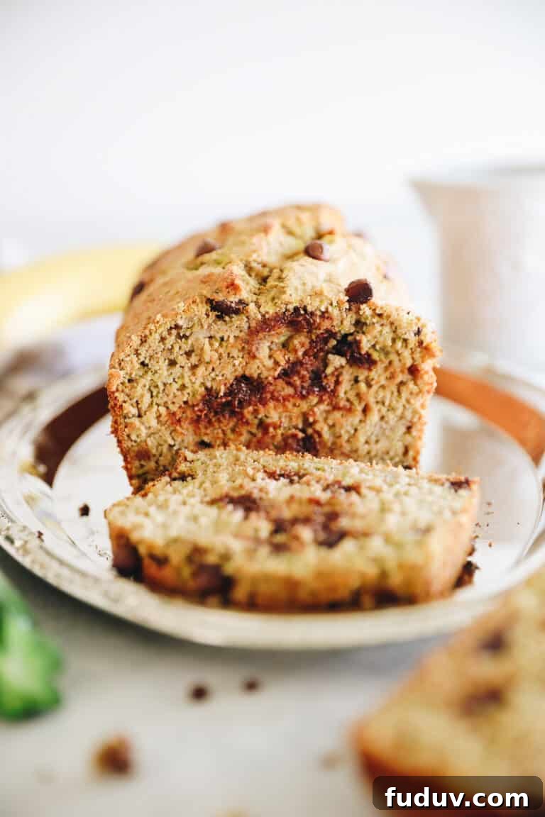 Loaf of zucchini banana bread sitting on a silver platter. One slice of bread laying in front of loaf.
