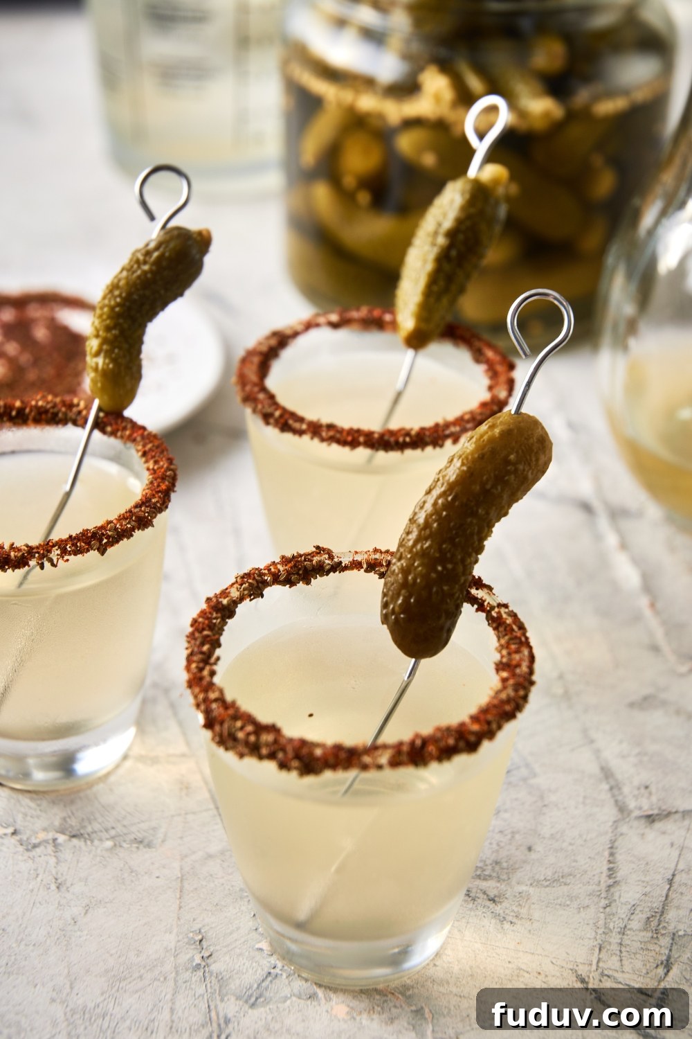 A few shot glasses with pickle shots and a garnished rim with a gerkin pickle.