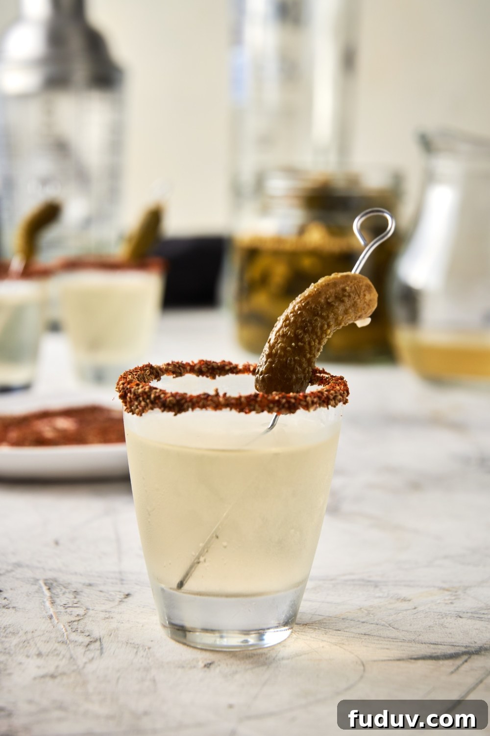 A shot glass with a pickle shot and a garnished rim with a gerkin pickle.