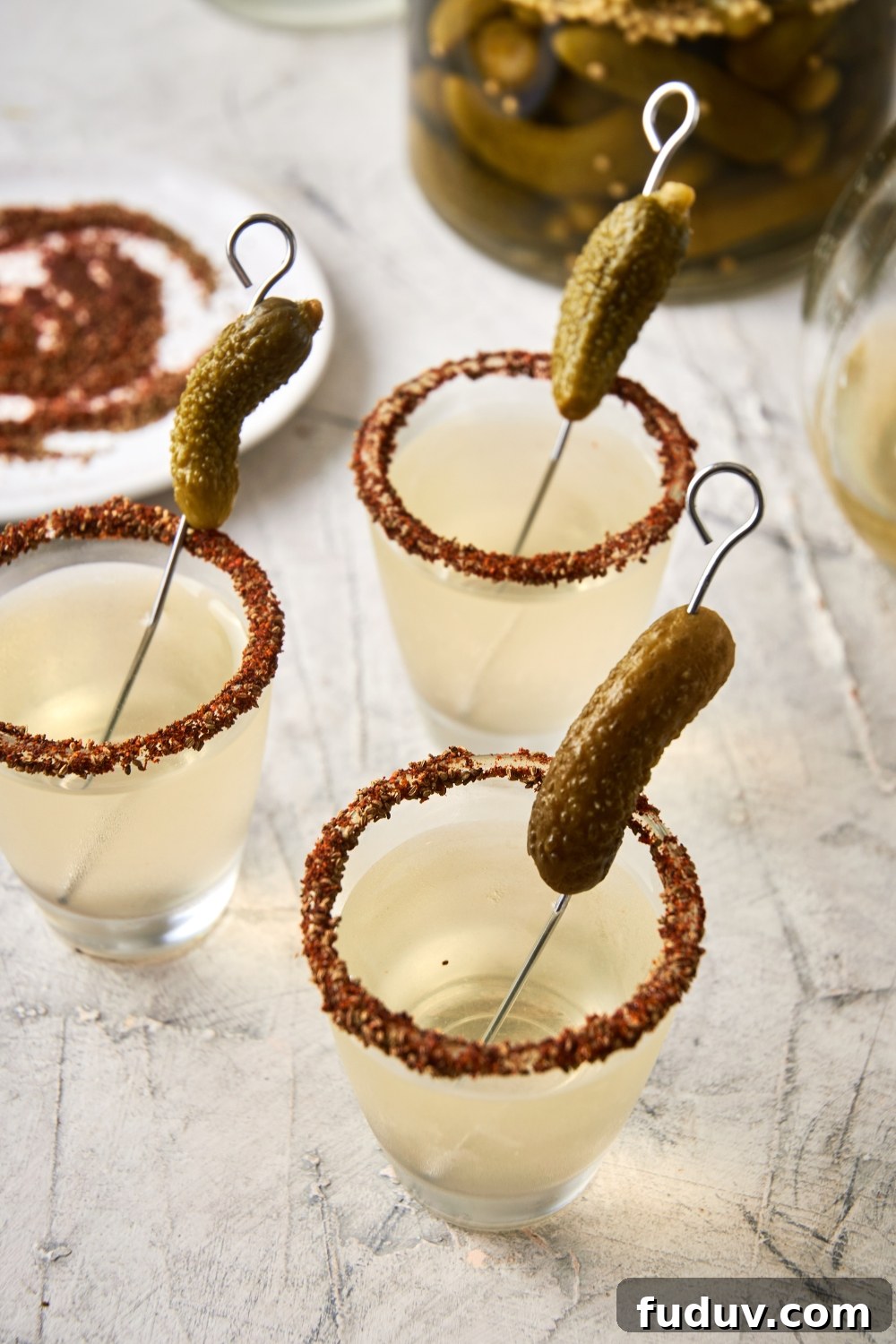A few shot glasses with pickle shots and a garnished rim with a gerkin pickle.
