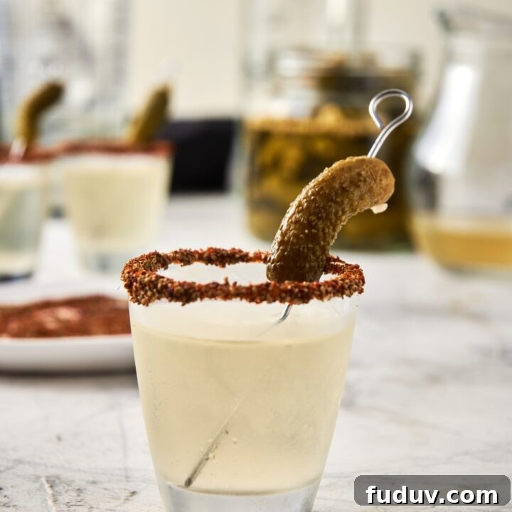 A shot glass with a pickle shot and a garnished rim with a gerkin pickle.