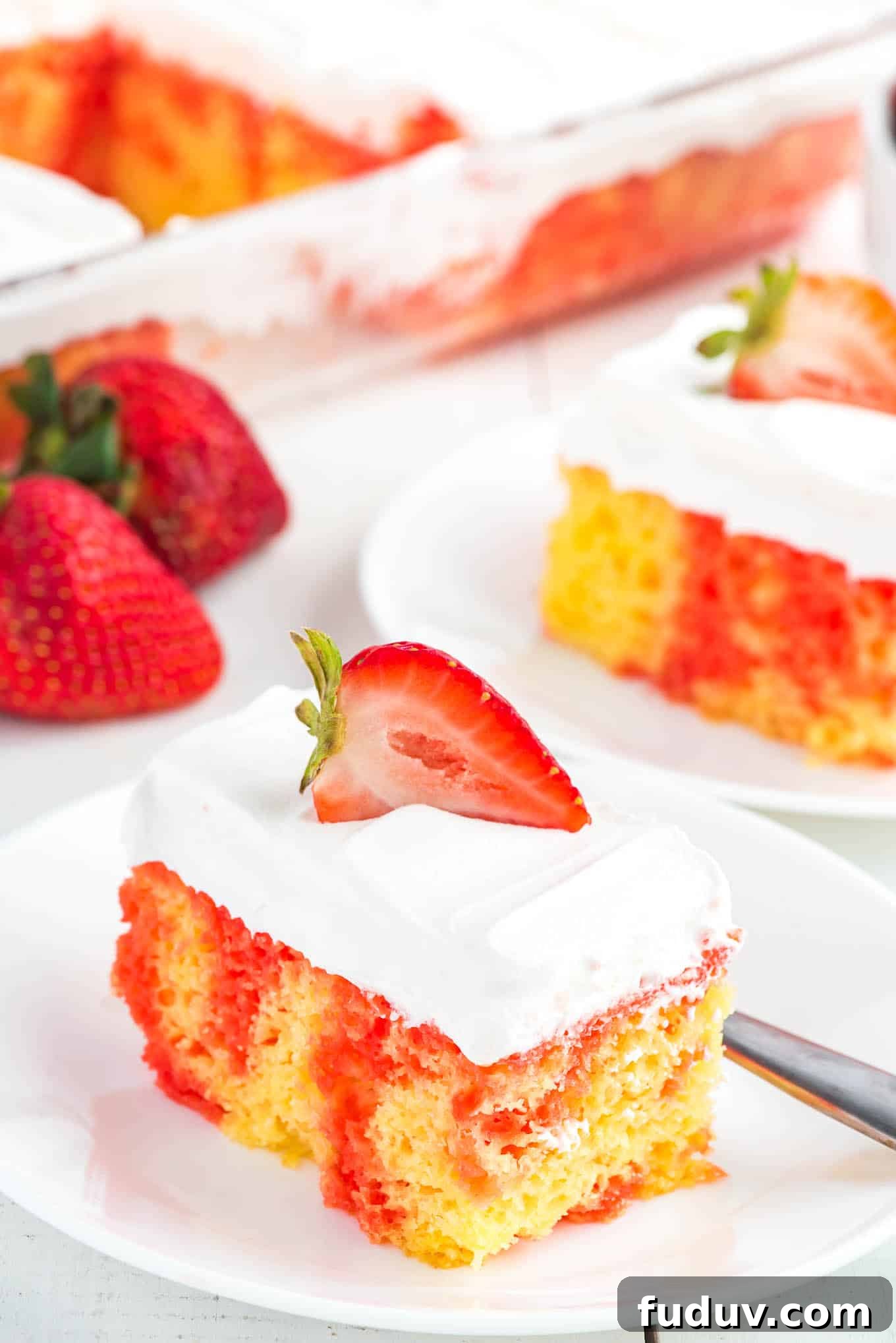 A square of jello poke cake topped with a strawberry half on a plate.